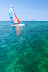 A sailboat sailing near a tropical island in summer.