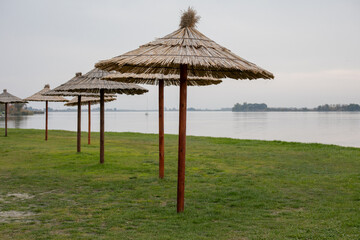 Thatched beach umbrellas line a serene lakeshore, evoking a peaceful retreat ideal for summer vacations or relaxation themes