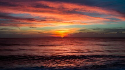 Obraz premium Dramatic sunset over the ocean with vibrant orange, red, and blue colors in the sky, reflecting on the calm water surface