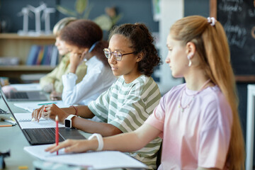 Side view of diverse group of children sitting in row in school classroom and using computer