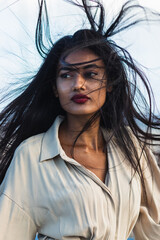 Beautiful indian woman with long, dark hair blowing in the wind, wearing a stylish light gray shirt