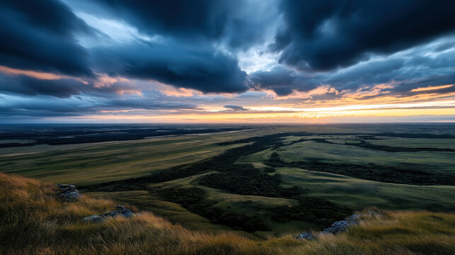 Panoramic view of a vast landscape with rolling grassy hills under dramatic cloudy sky during sunset