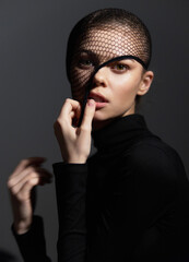 Mysterious young woman with fishnet headpiece, softly illuminated against a dark background, expressing intrigue and confidence through her gaze and subtle gestures.