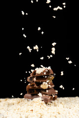 Nut shavings pouring on milk chocolate on a black background.