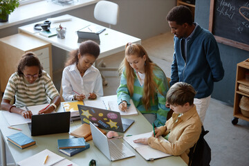 High angle view at diverse group of children working together sitting at big table in school...