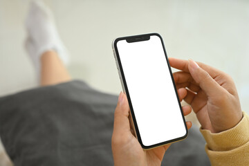 Close up of female hands holding mobile phone with empty screen sitting on couch