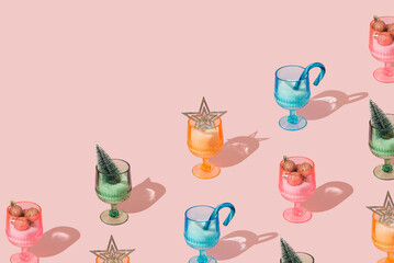 Christmas pattern made of colorful wine and cocktail glasses with snow and Xmas decorations on pastel pink background. Minimal Christmas and New Year party concept. Creative festive holiday backdrop.