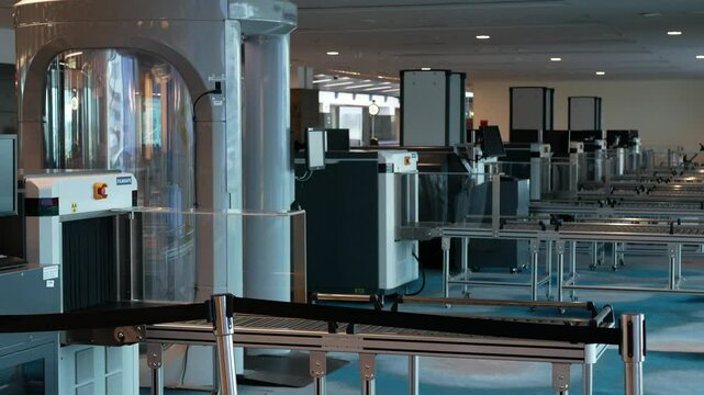 row of X-ray machines and body scanner for detecting prohibited items in luggage, bag at airport departure terminal hall security area without any staff and passenger
