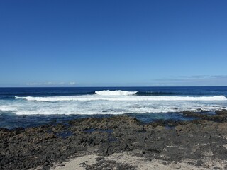 Ocean waves on rocky shore under blue sky
