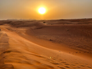 A mesmerizing desert landscape under a golden sunset, with rolling sand dunes stretching to the horizon. The warm glow creates a peaceful and timeless atmosphere across the arid terrain.