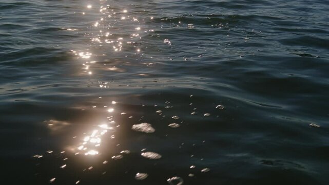 Sunlight reflection glimmering on water during sunset. Gentle waves rolling on a lake. 4K
