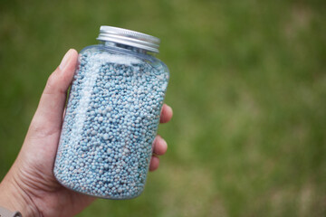Blue chemical fertilizers in a jar in hand on green grass background