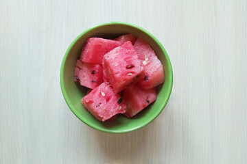 Red watermelon cubes in a green bowl on a white background. Top view.