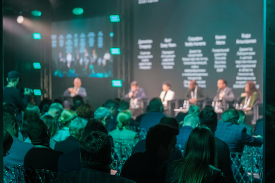 Audience attending business conference featuring diverse panelists discussing key industry topics in modern setting.