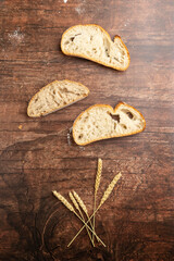 A rustic loaf of bread with slices is displayed on a dark slate board, accompanied by wheat stalks and a light cloth, evoking a cozy, artisanal kitchen scene.