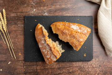 A rustic loaf of bread with slices is displayed on a dark slate board, accompanied by wheat stalks and a light cloth, evoking a cozy, artisanal kitchen scene.
