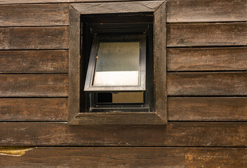An open window on a dark brown wooden wall, framed in black. The weathered wood exudes a rustic charm, captured from a low angle with a slightly blurred and muted color palette.