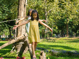 Cute sisters walking on a balance beam in an outdoor park. Children playing in the playground during summer vacation.