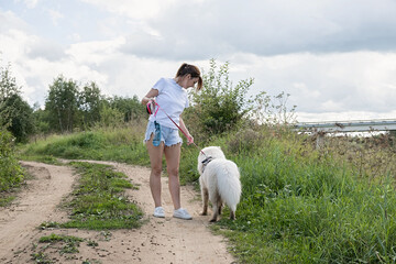 Young woman walking a white samoyed dog along a dirt road.