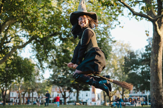 Cheerful woman flying with broom at Halloween park