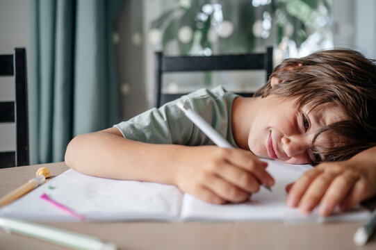 Tired boy leaning on table with book at home
