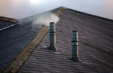 A frontal view of two galvanised metal chimney exhausts on a sloping slate roof
