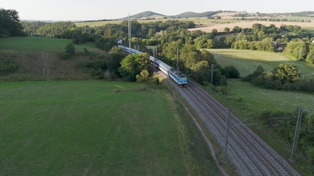 drone shot of a moving train in a typical Czech summer landscape on an electrified double-track track