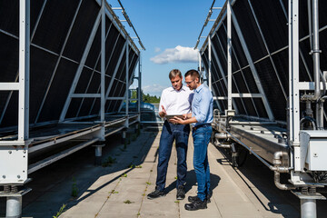 Two businessmen using digital tablet on rooftop beside refrigeration installation