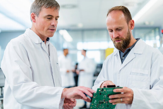Colleagues in electronics factory discussing over motherboard