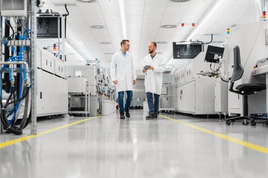 Discussing technicians walking through electronics factory holding digital tablet
