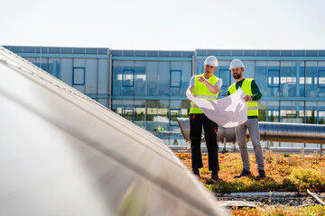 Two technicians studying plan on the roof of a company building with solar panels