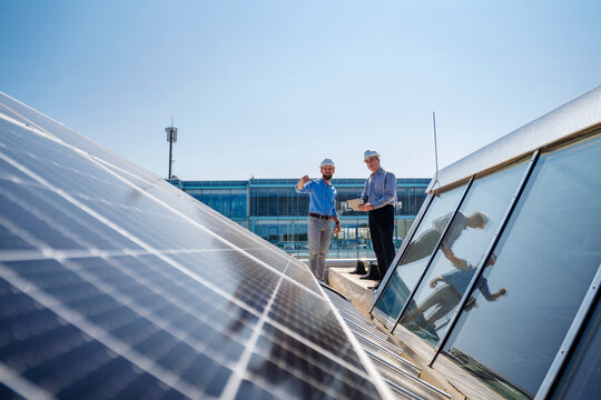 Two businessmen wearing hardhats having a meeting on the roof of a company building with solar panels