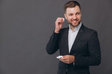 Handsome young business man in classic gray suit, shirt holding wireless earphones with charging...