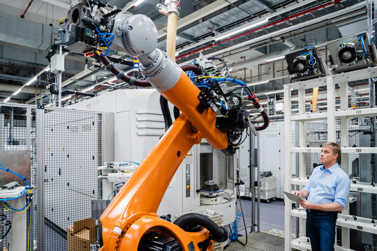 Businessman using digital tablet at industrial robot in a factory - Powered by Adobe