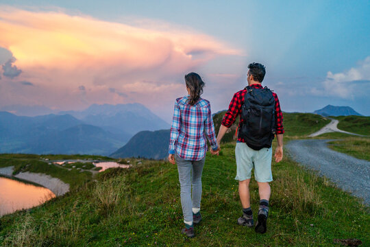 Backpacker holding hands of girlfriend and walking on mountain at sunset