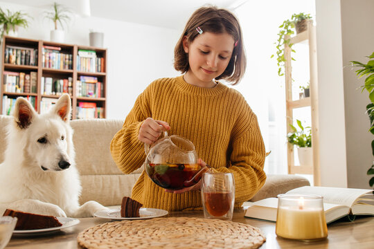 Smiling girl pouring herbal tea in glass near dog at home