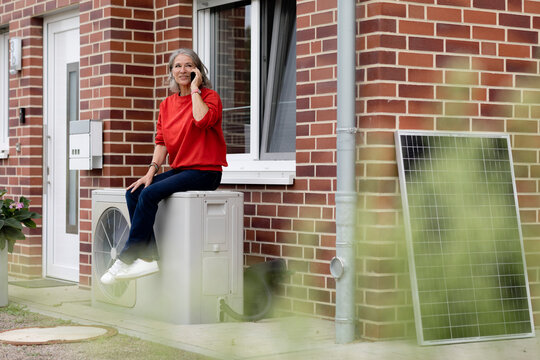 Senior woman talking through smart phone and sitting on heat pump