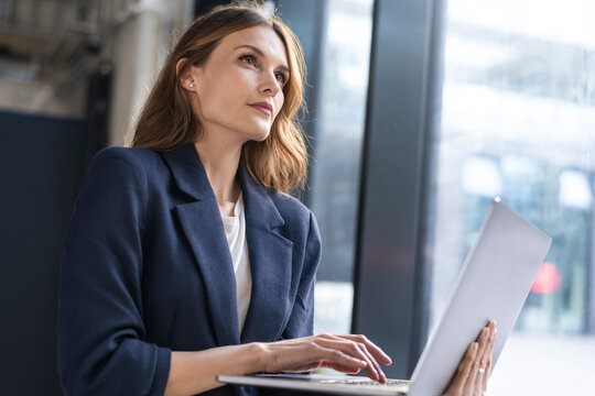 Thoughtful businesswoman using laptop in office - Powered by Adobe