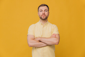 Cute unshaven man with crossed arms in yellow shirt posing isolated on yellow background with copy...