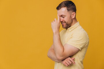 Cute unshaven man in yellow shirt putting hand on head and thinking and smiling isolated on yellow...
