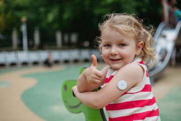 Little girl with diabetes giving thumbs up playing on seesaw on playground