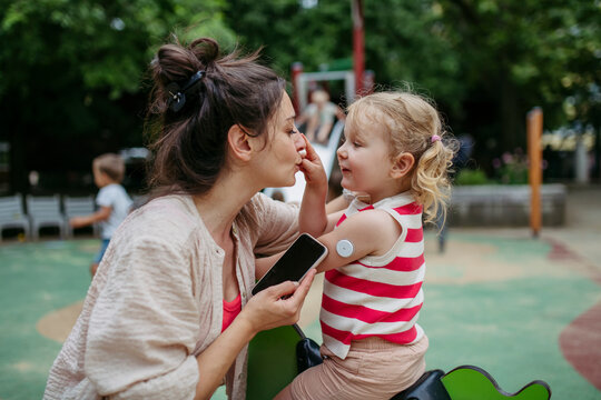 Mother with smartphone checking on little girl with a continuous glucose monitor sensor on her shoulder