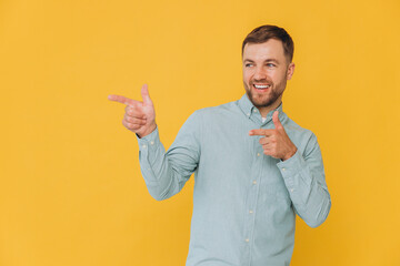 Cute unshaven man in mint shirt pointing fingers up at copy space isolated on yellow background