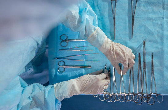 Hands of nurse arranging surgical scissors on operating table