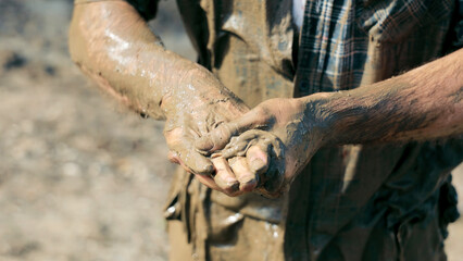 Close-up of hands covered in wet mud. Close-up of a person's hands coated in thick, wet mud, capturing a raw and rugged scene of outdoor labor or recreation.