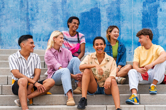 Multi ethnic group of young people sitting on steps in front of wall
