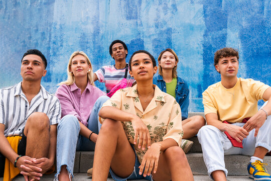Confident young people sitting on steps in front of wall