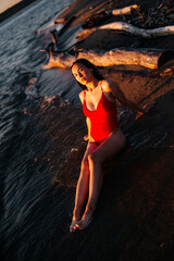 A girl in a red swimsuit lies on the beach at sunset