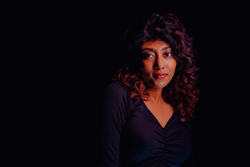 Naklejka premium A woman with dark hair and a black shirt is standing in front of a black background. She has a serious expression on her face