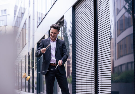 Smiling businessman playing with yo-yo near office building